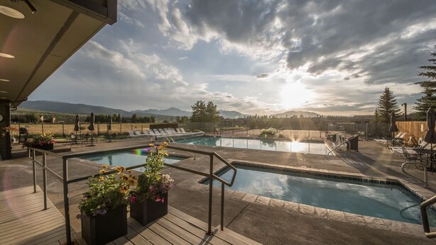 A rooftop pool with two separate sections, surrounded by lounge chairs and umbrellas, with mountains in the background. - Recently Renovated- Perfect for a Family Getaway! (Fraser)