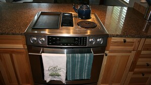 A kitchen with a stainless steel stove, a digital clock, and a kettle on the counter. - Recently Renovated- Perfect for a Family Getaway! (Fraser)