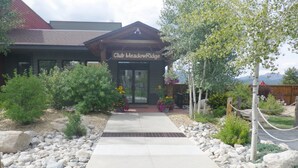 A building labeled "Club MeadowRidge" with a paved walkway leading to the entrance, surrounded by rocks and plants. - Recently Renovated- Perfect for a Family Getaway! (Fraser)