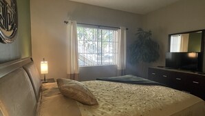 Ein Schlafzimmer mit einem Bett, Deckenventilator, einem Vorhangfenster, einem Fernseher und einer Pflanze.