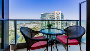 A balcony with two wicker chairs and a small table, overlooking a cityscape with modern buildings and a bridge. - Elegant Downtown Oasis with City and Lake Views Plus Parking! (Old Toronto)