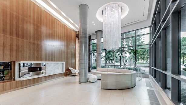 A spacious lobby with a large chandelier, a round seating area, and large windows offering a view of the outdoors. - Elegant Downtown Oasis with City and Lake Views Plus Parking! (Old Toronto)