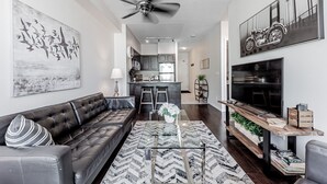 A modern living room with a sofa, a coffee table, and a TV. There is a kitchen in the background with a fridge and a microwave. - Elegant Downtown Oasis with City and Lake Views Plus Parking! (Old Toronto)