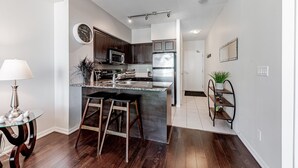 A modern kitchen with dark wood cabinets, stainless steel appliances, and a granite countertop. There is a clock on the wall and a small plant on the countertop. - Elegant Downtown Oasis with City and Lake Views Plus Parking! (Old Toronto)