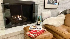 A cozy living room with a fireplace, a leather sofa, and a Scrabble game box on an ottoman. - Bloomington Indiana Rental- Entire House - 5 Bedrooms and 3 full bathrooms (Bloomington)