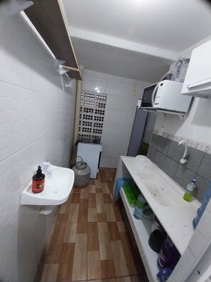 Uma cozinha compacta com azulejos brancos, pia, botijão de gás e micro-ondas.