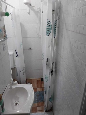 Uma casa de banho pequena com uma pia branca, um chuveiro com cortina estampada com padrão de folha e chão em mosaico.