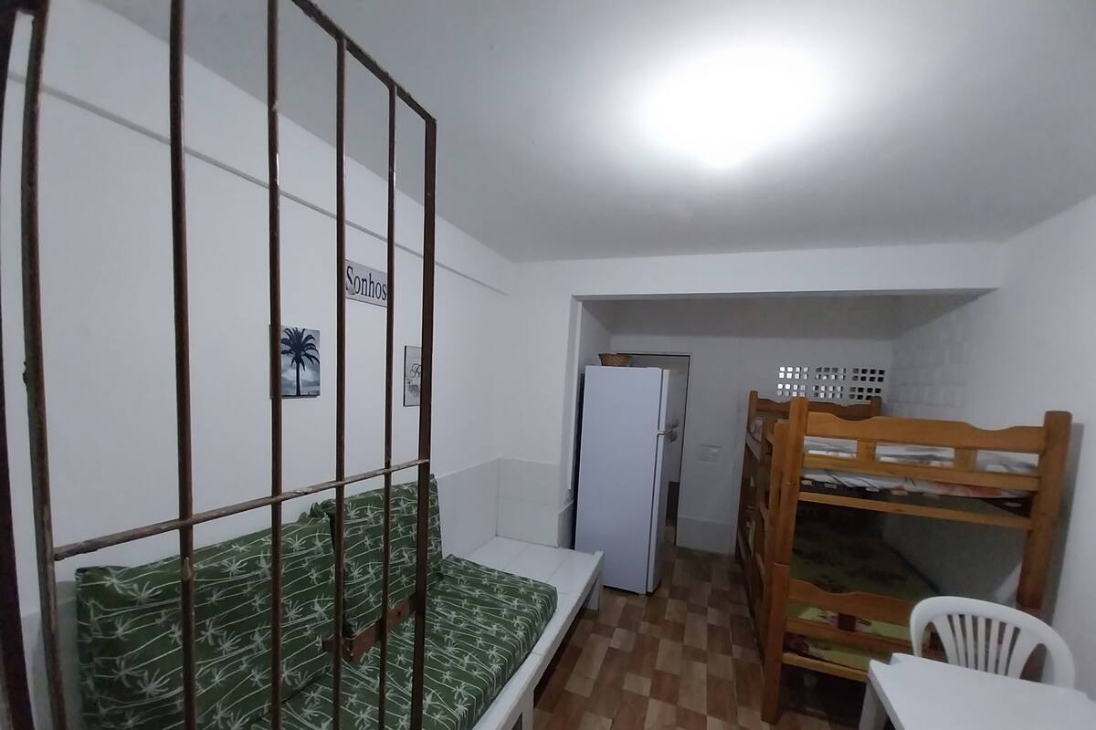 Pieni, kompakti huone, jossa on kerrossängyt, yksi sänky kuviollisella patjalla, valkoinen jääkaappi ja pieni pöytä tuolilla.