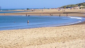 A wide sandy beach with clear blue water, people walking, and a distant hill with structures. - 6 Berth Comfy Homely Caravan, Dog Friendly (Burgh Castle)