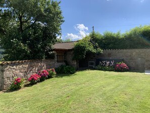 Guesthouse with entrance, surrounded by a well-maintained garden and a large tree.