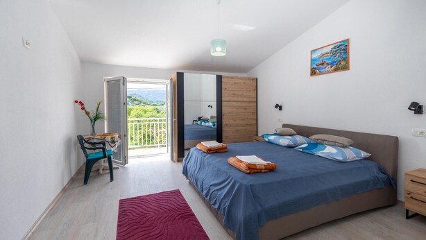 A modern bedroom with a large bed, a balcony with a view, and a dining area with a table and chairs. - Amazing home in Peracko Blato (Peracko Blato)