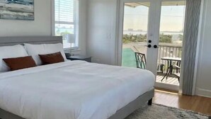 A bedroom with a large bed, a ceiling fan, a view of the outdoors through a sliding glass door, and a painting on the wall. - Stunning 4/3 w/ Heated Pool, Water View & Arcade! (Jensen Beach)