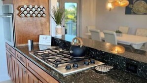 A modern kitchen with a central island, wooden cabinets, a gas stove, and pendant lighting. - Stunning 4/3 w/ Heated Pool, Water View & Arcade! (Jensen Beach)