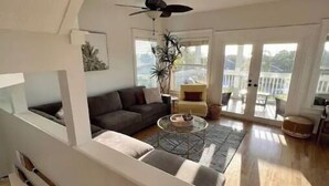 A spacious living area with a ceiling fan, a sofa, a coffee table, and a balcony with large windows. - Stunning 4/3 w/ Heated Pool, Water View & Arcade! (Jensen Beach)
