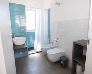 A bathroom with a white sink, a bidet, a toilet, and a shower curtain. - Modern and brand new apartment in villa five minutes from the sea and downtown (Avola. SR)