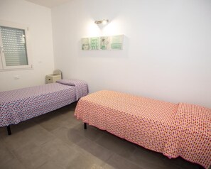 A room with two single beds, a small bedside table, a wall-mounted light, and a window with blinds. - Modern and brand new apartment in villa five minutes from the sea and downtown (Avola. SR)