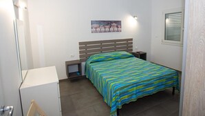 Ein Schlafzimmer mit Bett, Nachttischen, einem Schreibtisch und einem Fenster mit Jalousien.