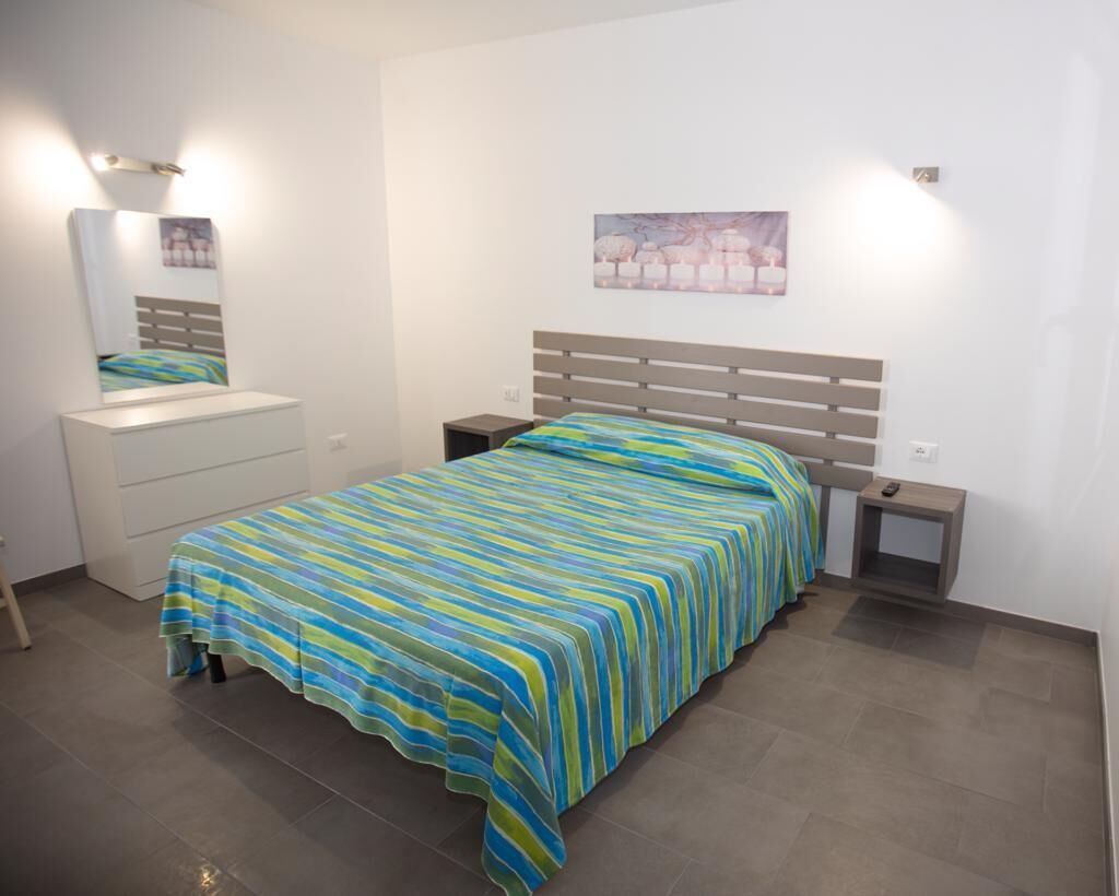 A bedroom with a bed, a nightstand, a dresser, and a wall-mounted light fixture.
