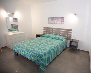 A bedroom with a bed, a nightstand, a dresser, and a wall-mounted light fixture. - Modern and brand new apartment in villa five minutes from the sea and downtown (Avola. SR)