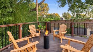 A deck with four wooden chairs and a central fire feature.
