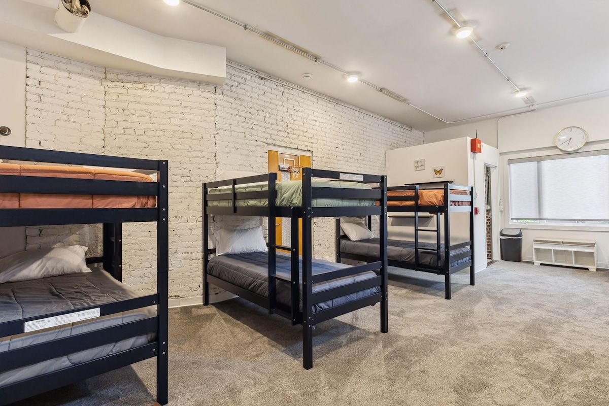 A room with bunk beds, a white brick wall, a clock, and a window.