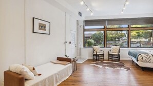 A modern, well-lit room with a bed, two chairs, a small table, and a large window offering a view of the outdoors. - Over 4500 sqft of Luxury living [Billiards table, Arcade room, 5 BR & 4 BA] (Cleveland)