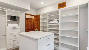 Ein begehbarer Kleiderschrank mit offenen Regalen, einer zentralen weißen Kommode und einer Holztür.