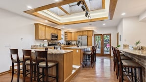 A spacious kitchen with wooden cabinets, a central island with bar stools, and a skylight above. - Over 4500 sqft of Luxury living [Billiards table, Arcade room, 5 BR & 4 BA] (Cleveland)