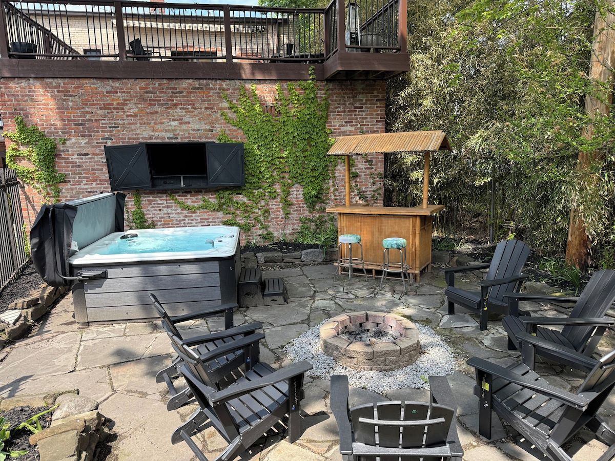 An outdoor patio with a hot tub, fire pit, and seating area.