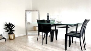 A dining area with a glass table and black chairs, a potted plant, and a mirror on the wall.