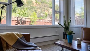 A room with a large window, a sofa, a table with a lamp, and two potted plants.