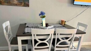 Una mesa de comedor con cuatro sillas blancas, un florero con flores azules y un mantel a rayas.