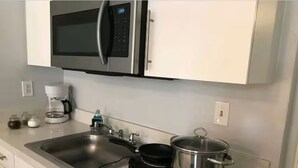 Una cocina equipada con un lavamanos de acero inoxidable, un microondas, una cafetera y una estufa portátil.