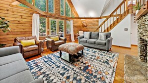 A spacious living room with a high ceiling, wooden walls, and large windows. There are multiple seating areas with sofas and a patterned rug. - Pet Friendly, Resort Access, Private! - Catahoula Cabin by Carolina Properties (Lake Lure)