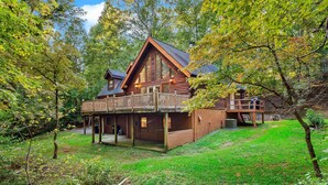 A log cabin with a balcony, surrounded by trees and a grassy yard. - Pet Friendly, Resort Access, Private! - Catahoula Cabin by Carolina Properties (Lake Lure)