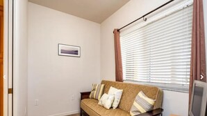Una sala de estar con un sofá color beige, un cuadro en la pared y una ventana con persianas.