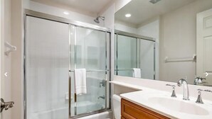 Un baño moderno con cabina de ducha acristalada, un espejo grande y un lavabo blanco con varios grifos.