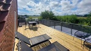 A wooden deck with outdoor furniture, a metal railing, and a view of greenery and distant buildings.