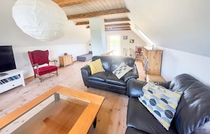 Una sala de estar con un sofá de cuero negro, un sillón rojo, una mesa de centro de madera y un mueble bajo para televisión blanco.