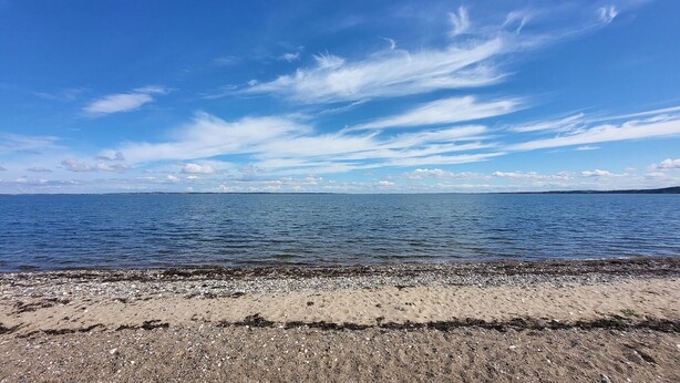 A beach with a clear sky, calm sea, and distant land.