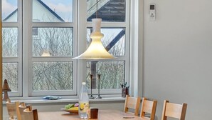 A dining area with a wooden table and chairs, a pendant light, and a window with a view of trees and a building.