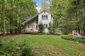 Escape to a cozy cabin nestled in a lush forest, featuring a spacious porch and a small deck area.