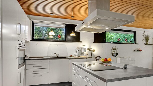 A modern kitchen with white cabinetry, a built-in oven, a large island with a sink, and a window with a view of greenery. - Lovely home in Højslev with WiFi (Højslev)