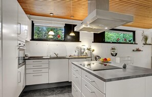 Een moderne keuken met witte kasten, een inbouwoven, een groot eiland met een spoelbak en een raam met uitzicht op groen.