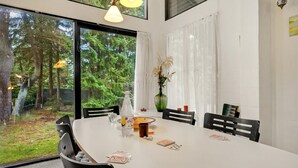 A dining area with a large table, chairs, and a view of a forest through large windows. - Lovely home in Højslev with WiFi (Højslev)