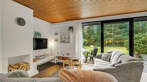 A modern living room with a flat-screen TV, a fireplace, a dining area, and a large window overlooking a garden. - Lovely home in Højslev with WiFi (Højslev)