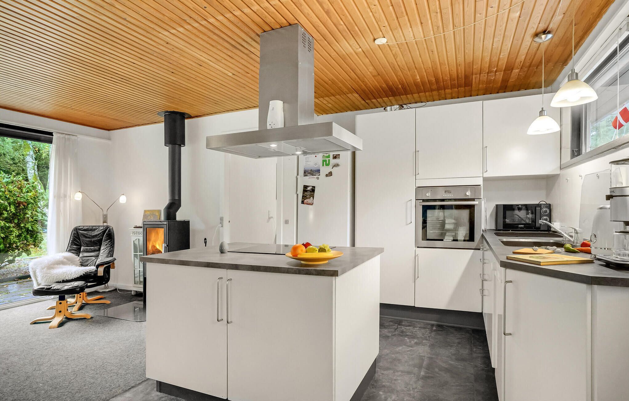 Una cocina moderna con armarios blancos, una isla central, una estufa y un ventanal amplio.