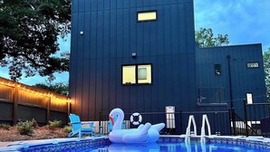 Une piscine avec un flotteur en forme de cygne et une chaise bleue, entourée d’une clôture en bois et illuminée de guirlandes lumineuses.
