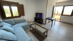 A living room with a light blue sofa, a glass coffee table, a TV on a stand, and a window with wooden shutters.