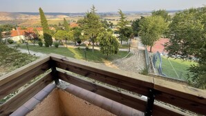 A view from a balcony overlooking a park with trees, a running track, and distant hills.